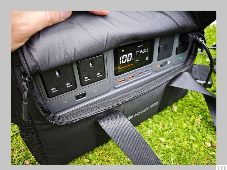Large grey device with outlets and small screen, tucked into a partially opened thick padded carrying bag